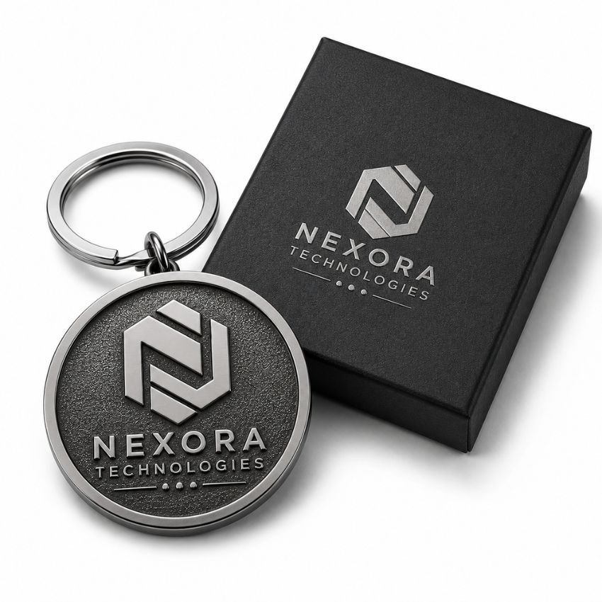 Custom Nexora Technologies logo round metal keychain with texture alongside a matte black gift box.