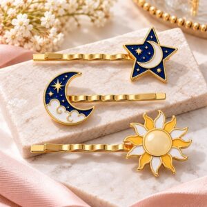 Gold enamel celestial hair clips featuring white and navy blue star, crescent moon, and sun designs on a marble display slab