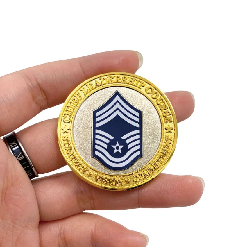 Hand holding a custom gold Chief Leadership Course challenge coin, highlighting the detailed texture and rank insignia.
