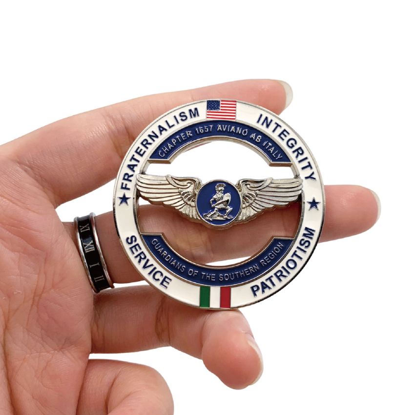 Handheld view of custom military challenge coin with cut-out design, showing the Aviano AB Chapter 1657 insignia side.