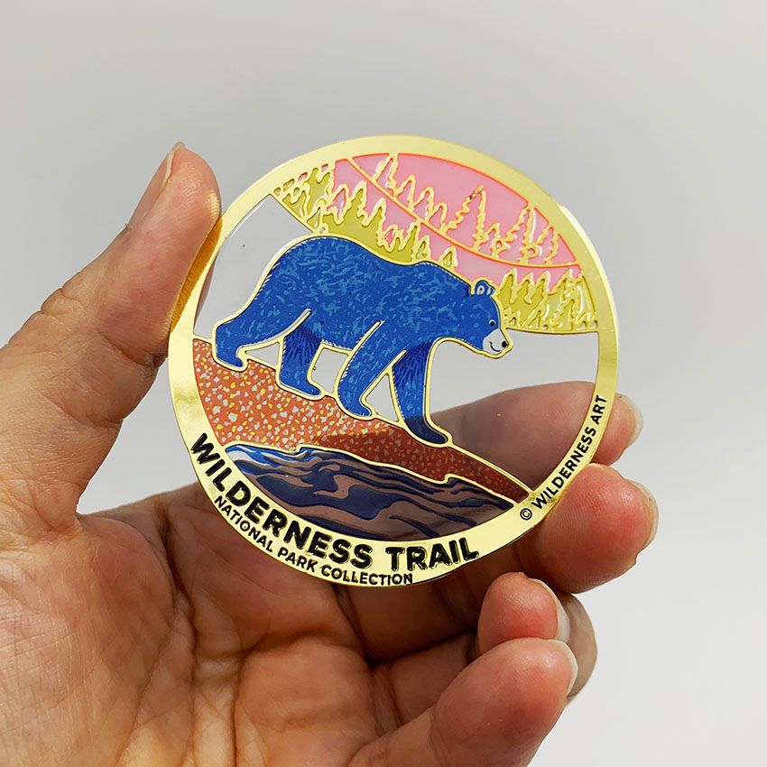 Hand holding a translucent Wilderness Trail enamel bookmark with UV printed details, demonstrating light-transmitting effect.