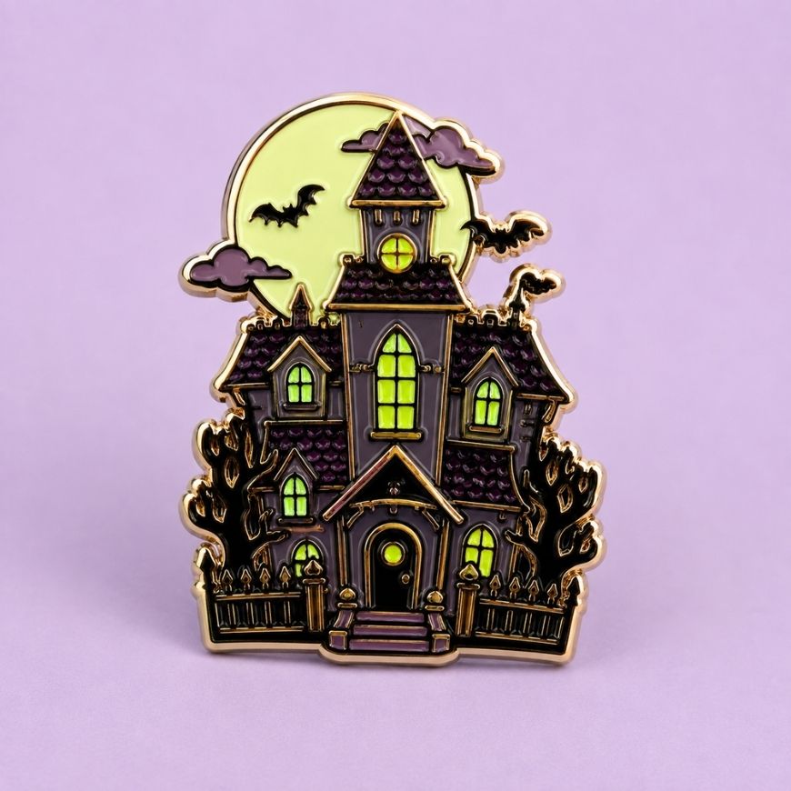 Detailed haunted house enamel pin with glowing windows and bats, custom Halloween souvenir and collectible badge.