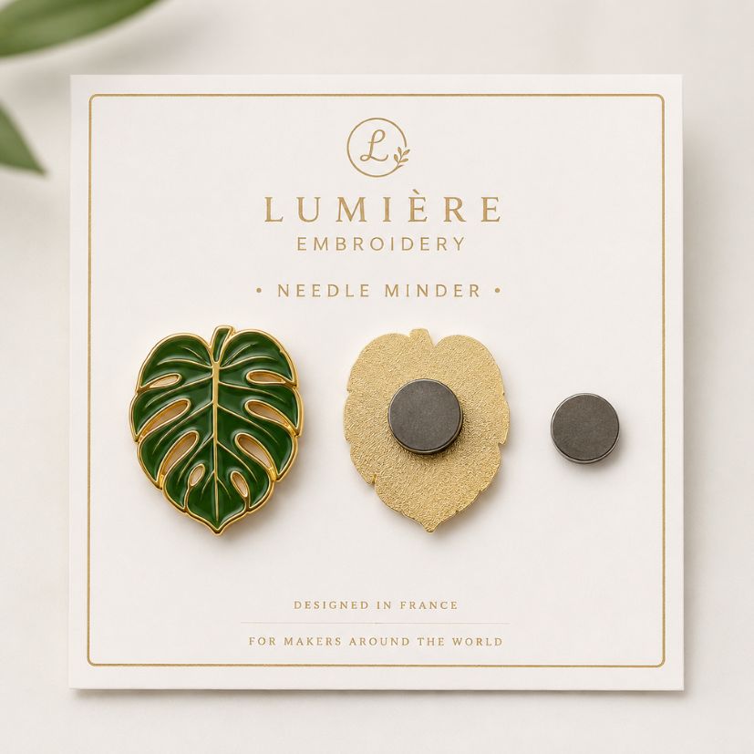 Monstera leaf enamel needle minder with attached back magnet and loose magnet on custom card packaging.