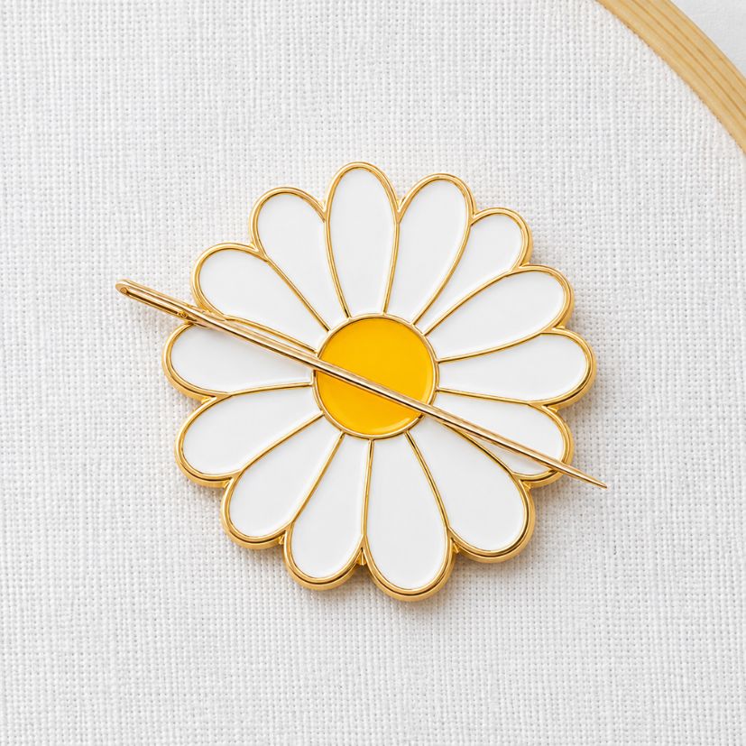 White daisy flower enamel needle minder with gold plating holding a needle, bulk craft and sewing supply order.